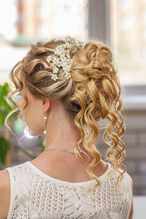 Hochgesteckte Brautfrisur mit herabfallenden Locken und Perlenapplikationen im Haar.