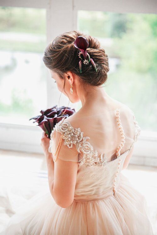 Klassisch hochgesteckte Brautfrisur mit Blüte im Haar.